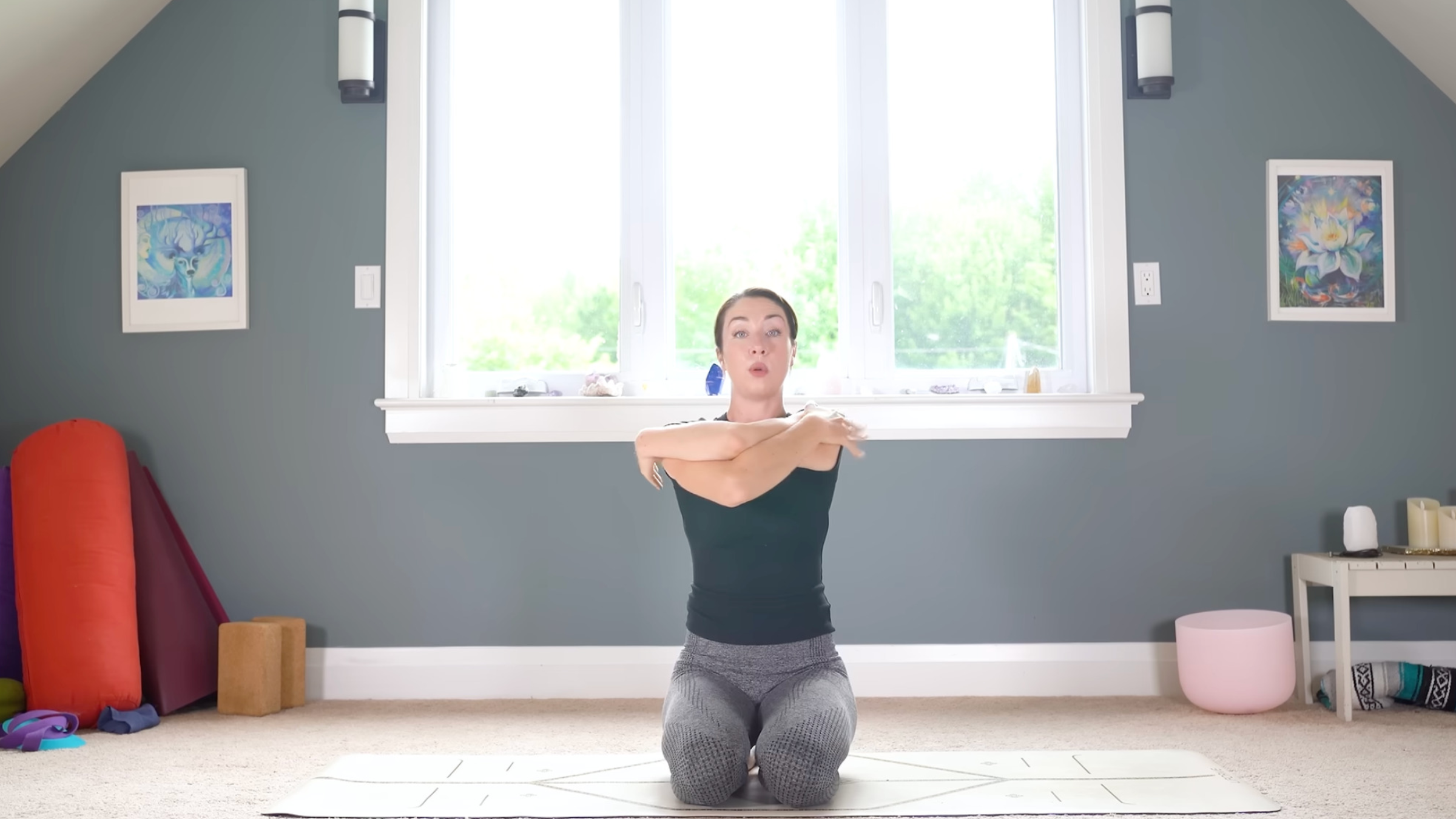 woman in yoga clothes kneeling on yoga mat with arms in an Eagle Arms variation with arms hugging themselves and elbows raised up in line with the shoulders