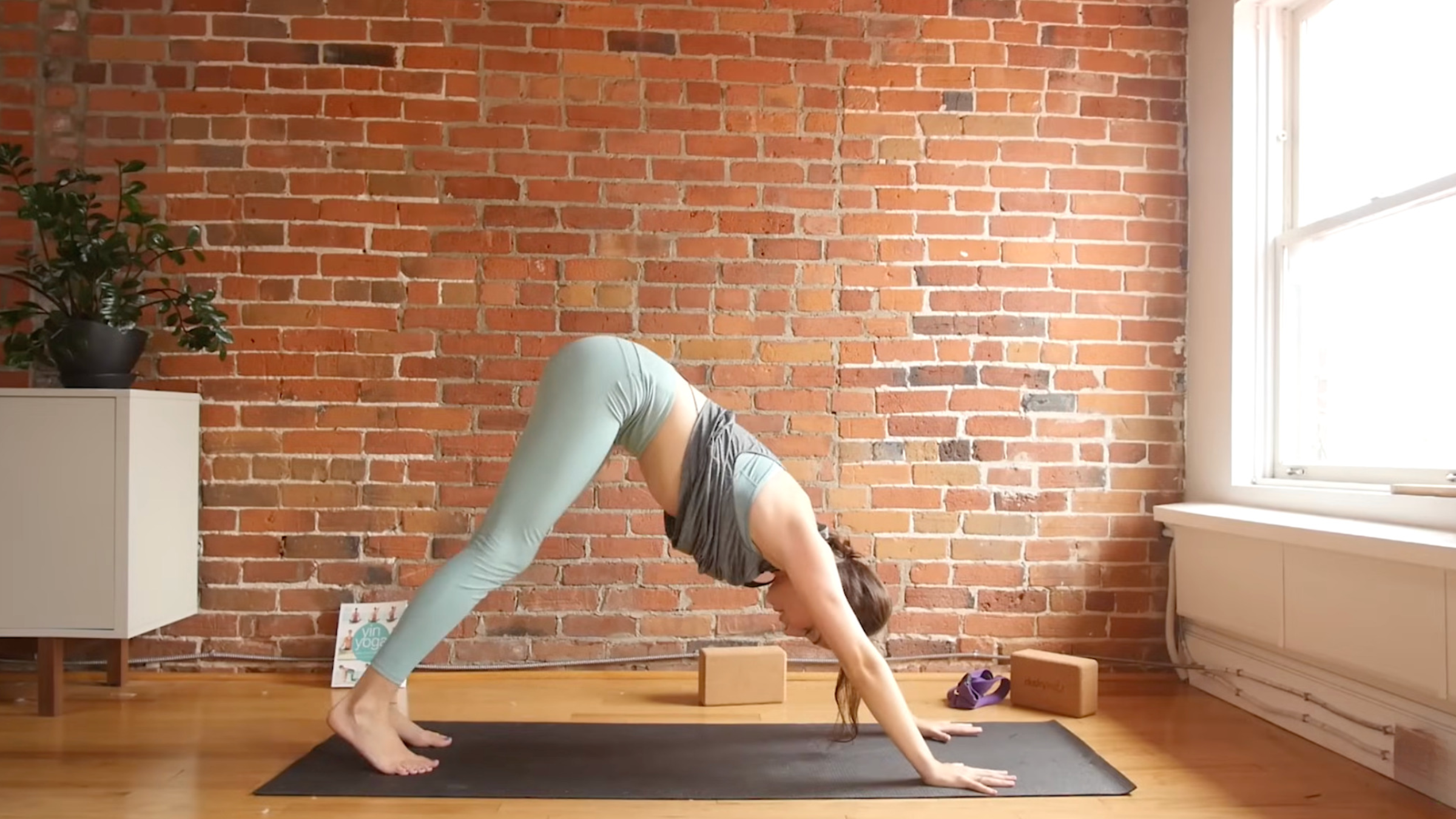 woman in yoga clothes on yoga mat in Downward-Facing Dog pose with hands and feet on mat and hips lifted high with flat back