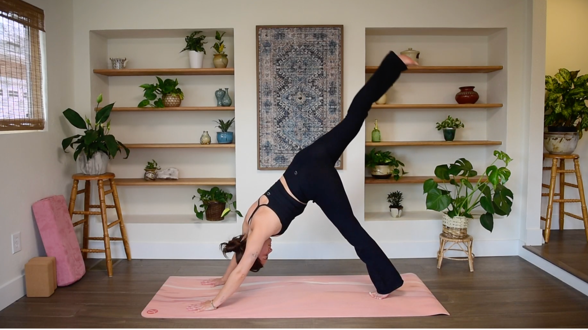 Caitlin K'eli in Downward-Facing Dog lifting one leg straight up toward the ceiling in Three-Legged Dog.