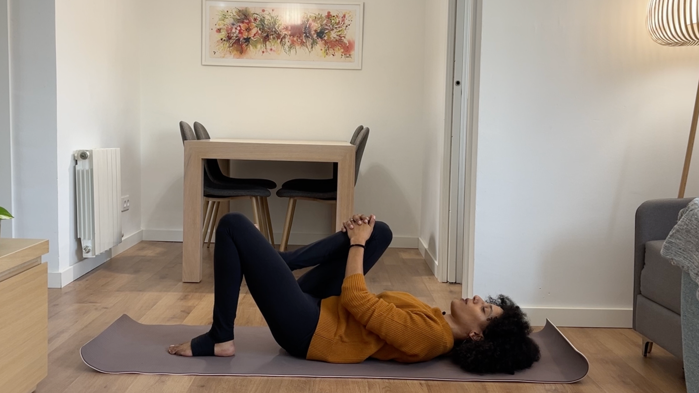Laia Bové lying on her back and gently drawing her right knee toward her chest with relaxed shoulders.
