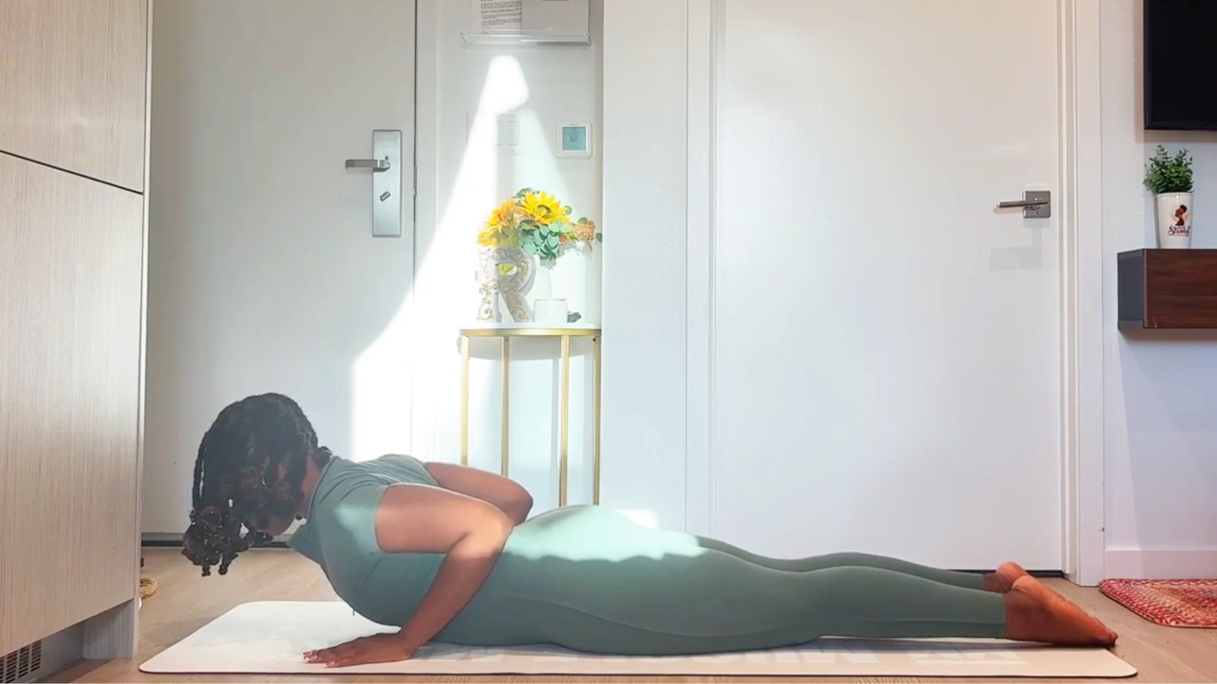 Ramoni Overton lying face-down on a yoga mat, pressing palms by chest to gently elevate chest into Baby Cobra pose.