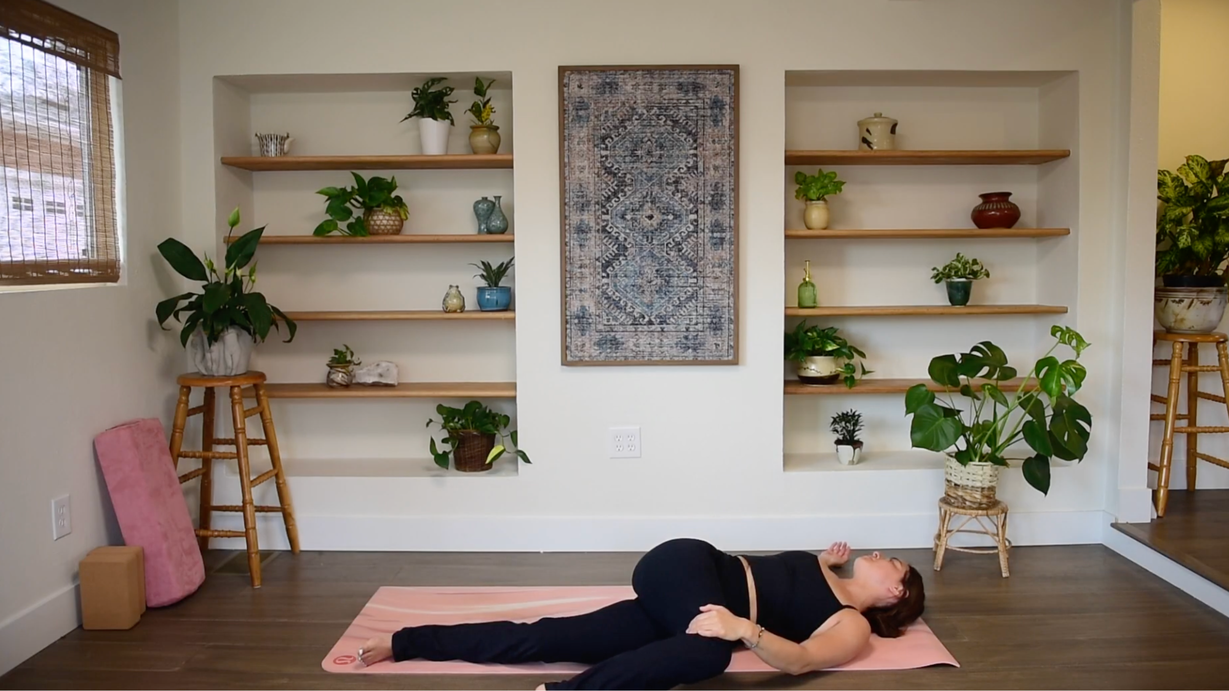 Caitlin K'eli lying on her back, drawing one bent knee across her body toward the floor in a Supine Spinal Twist.