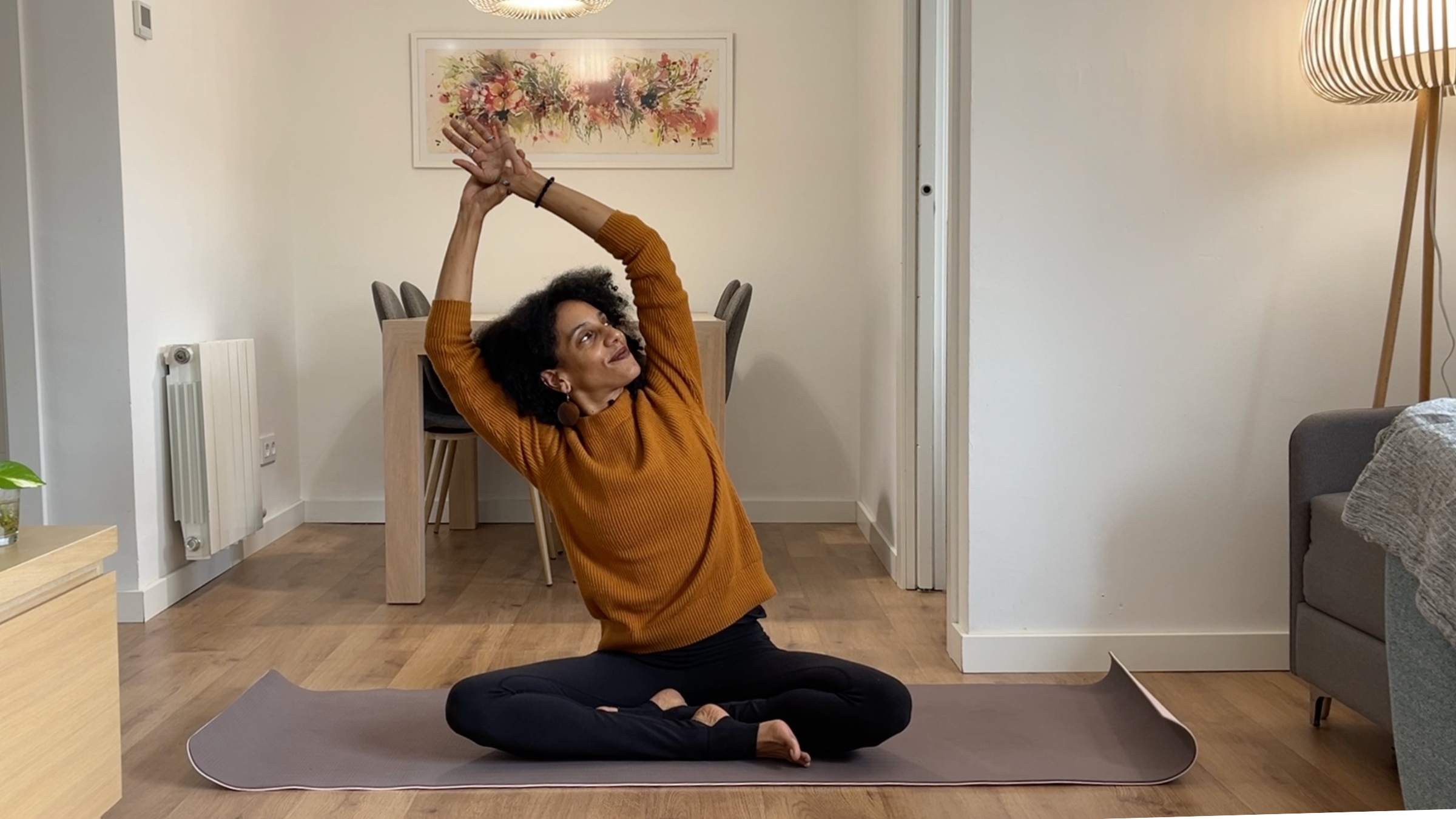 Laia Bové sitting cross-legged and reaching arms overhead while gently leaning laterally to stretch the side body.