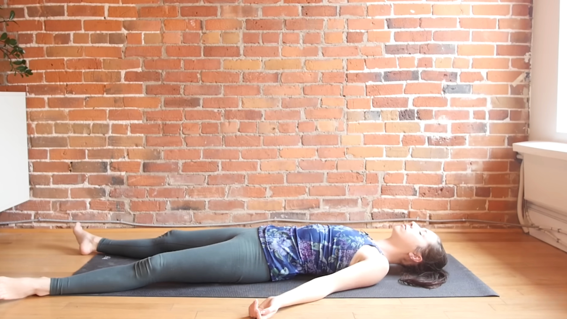 woman in yoga clothes lying on back in Savasana with legs and arms extended and relaxed