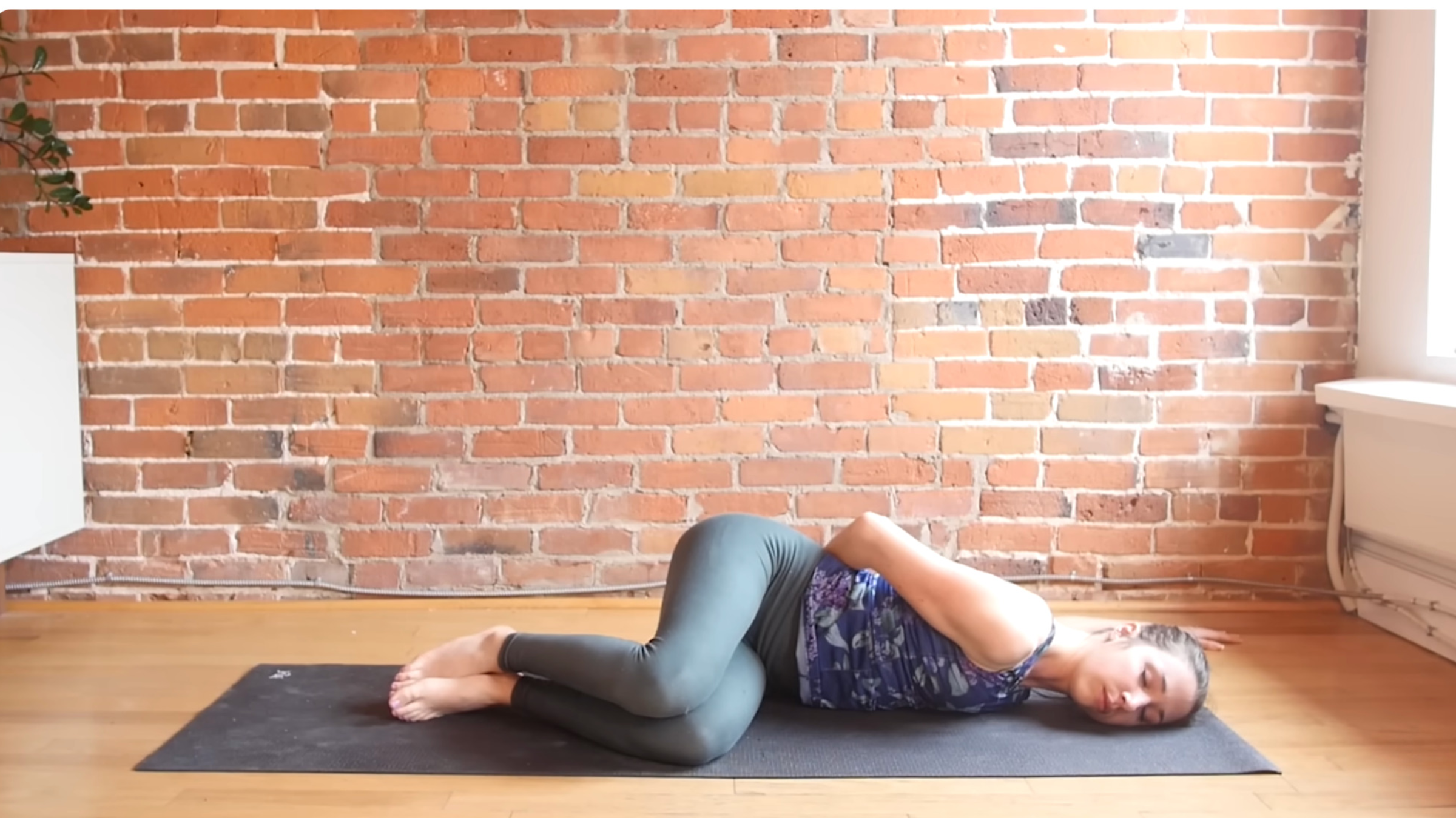 woman in lying chest opener with left arm behind her toward the left side of the mat while the rest of the body is lying on its left side toward the right side of the mat with knees bent