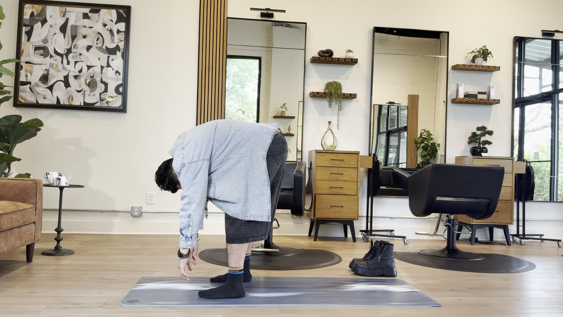 Yoga teacher standing at the front of his mat in Rag Doll or Standing Forward Bend (Uttanasana) with his arms reaching toward the mat