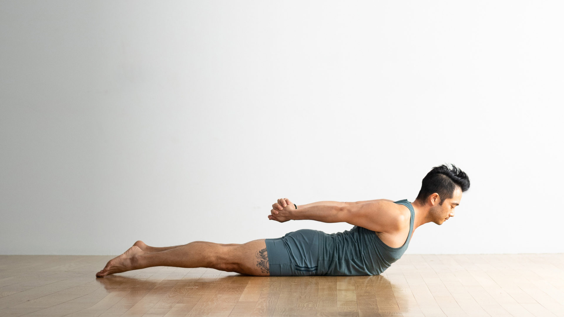 Many lying on his belly with his chest lifted and his hands interlaced behind his back in Locust Pose