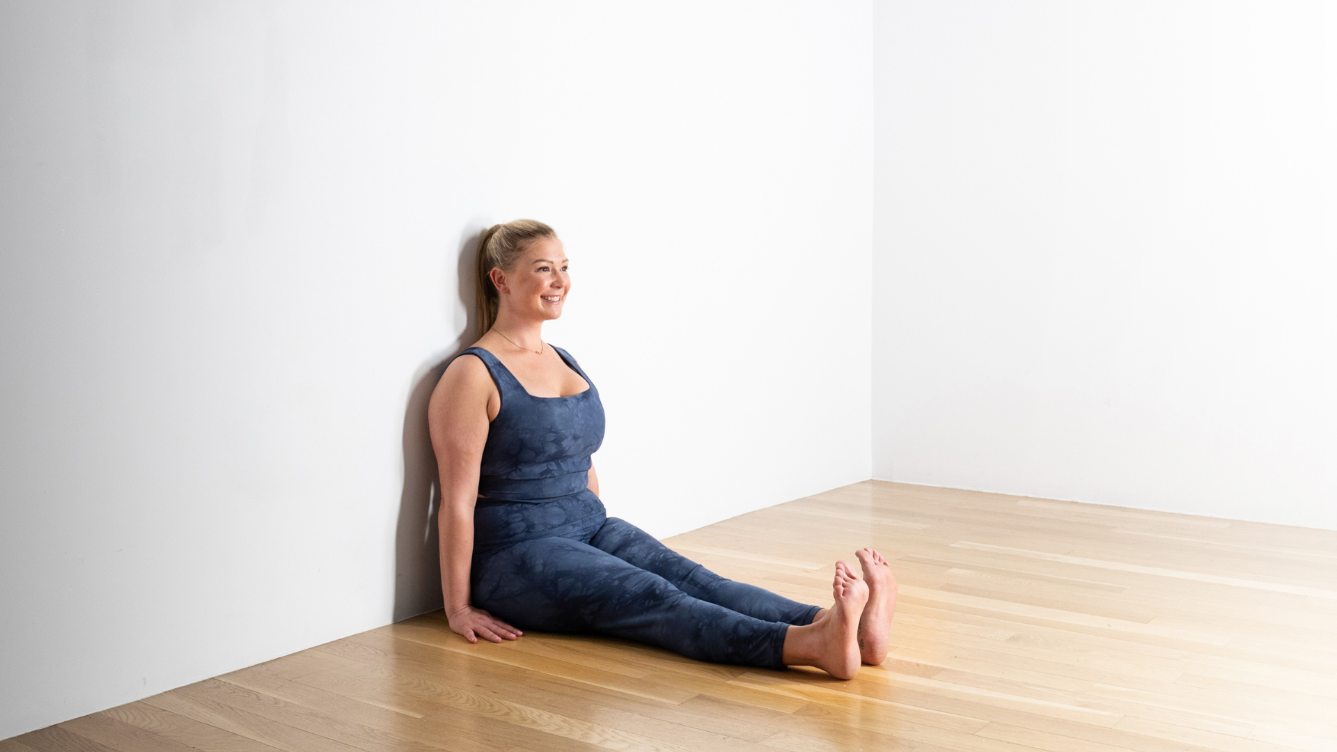 Woman sitting with her back against the wall in Staff Pose (Dandasana)